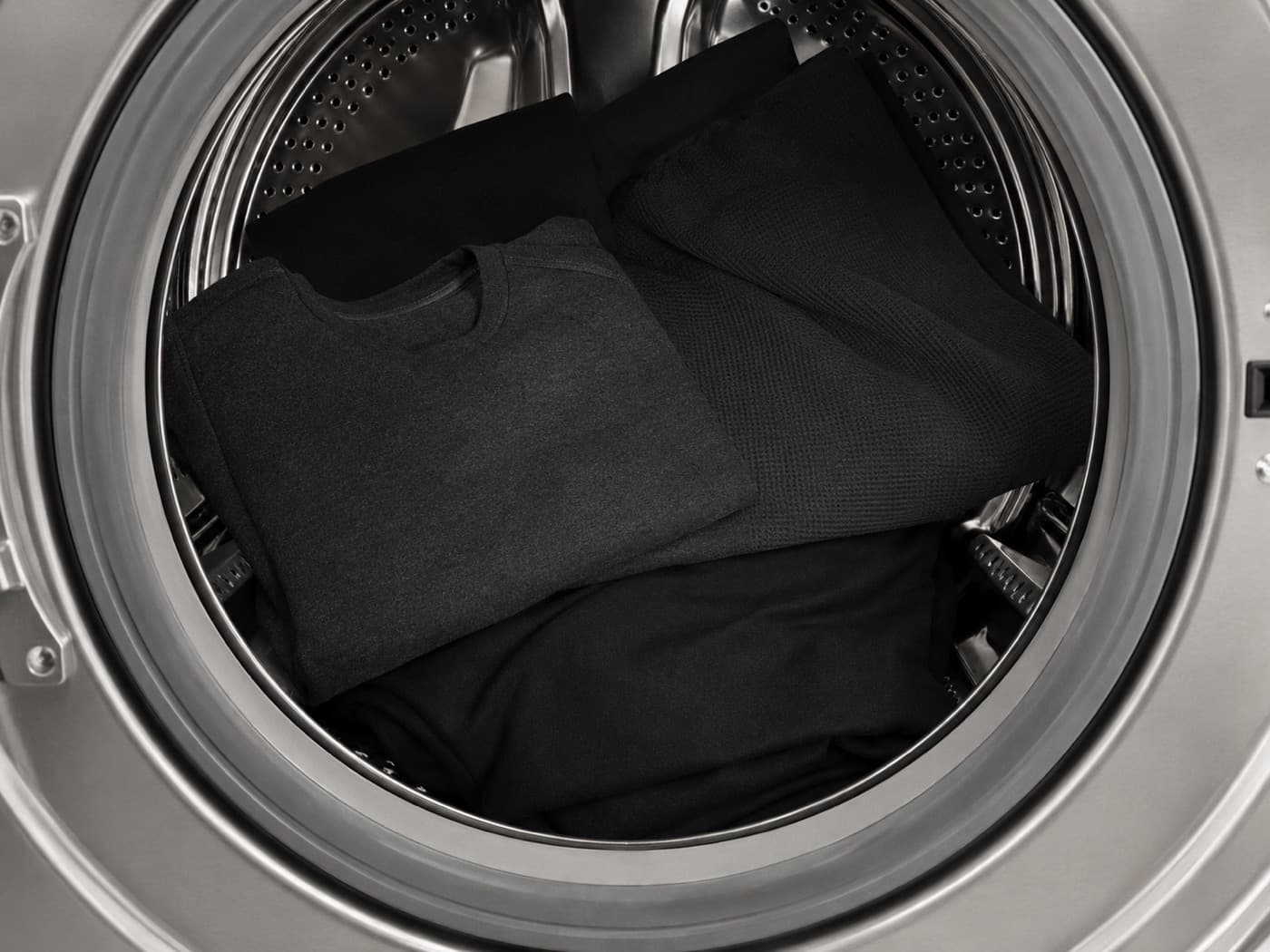 Looking down into an open stainless steel washing machine drum holding folded dark garments.