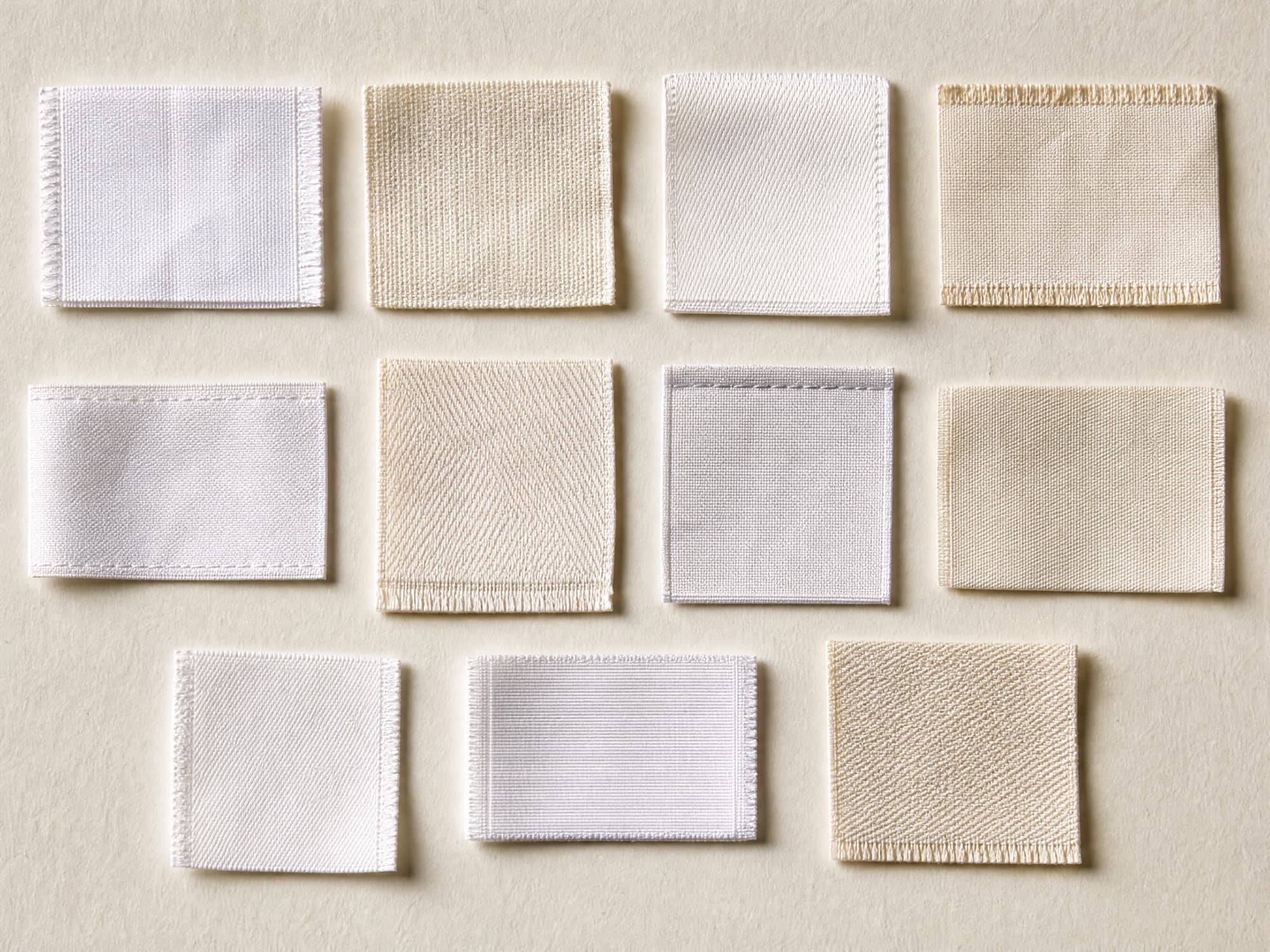 Eleven blank white and ivory garment care labels arranged in a specimen grid on warm off-white paper.