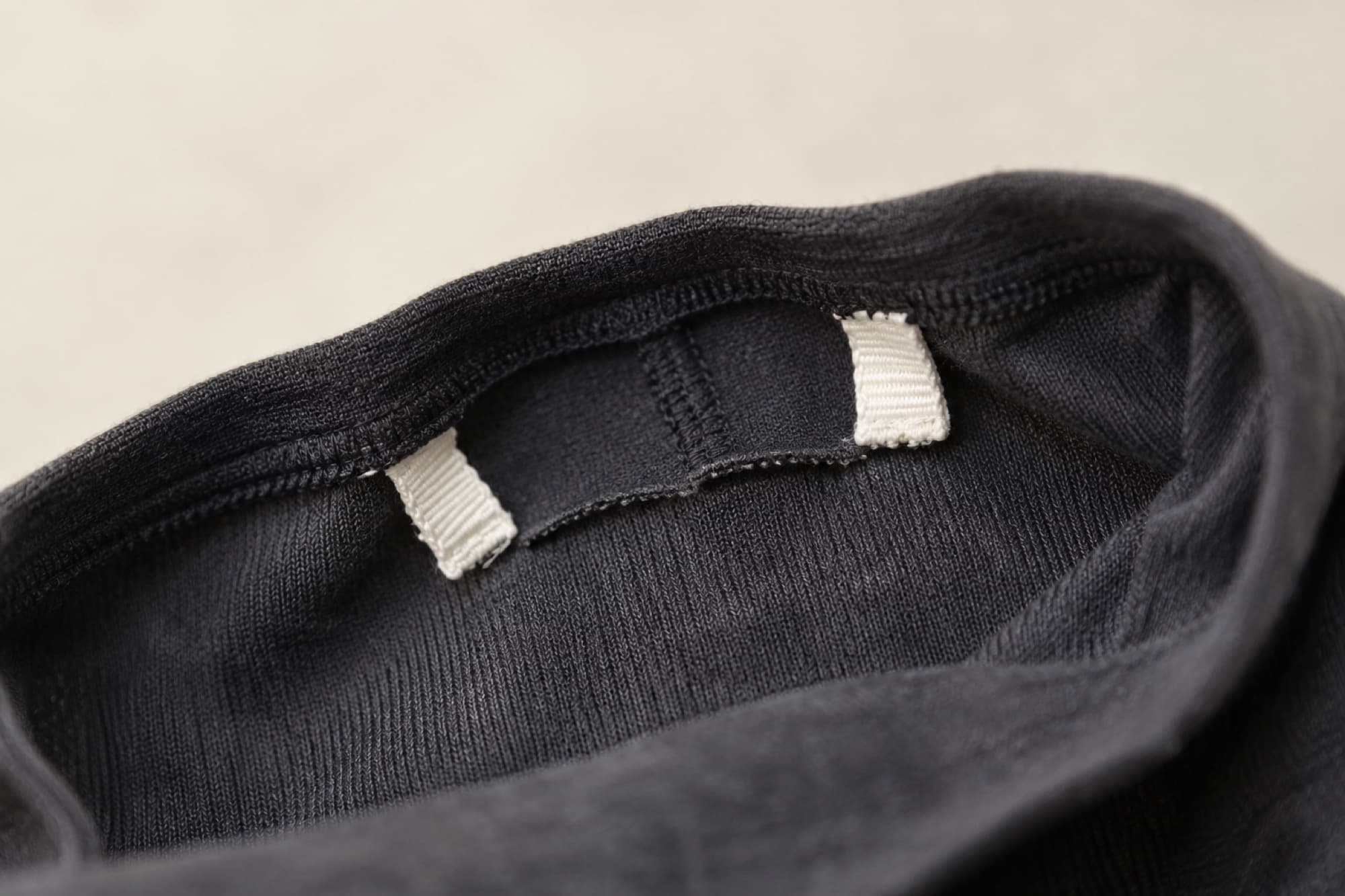 Close-up of a garment seam where the care label has been cut out, leaving two short stubs of white tape.