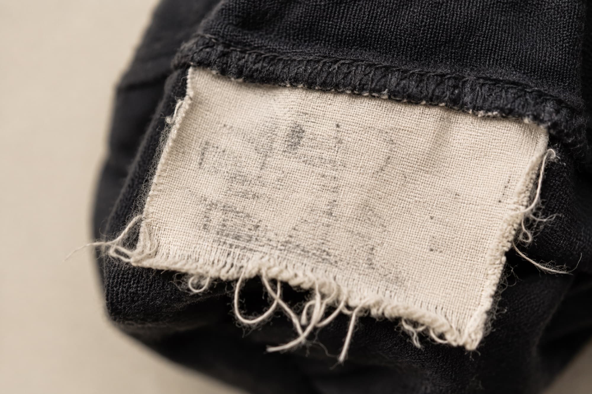 Macro photograph of a care label almost entirely worn away, with loose threads at the frayed edge.