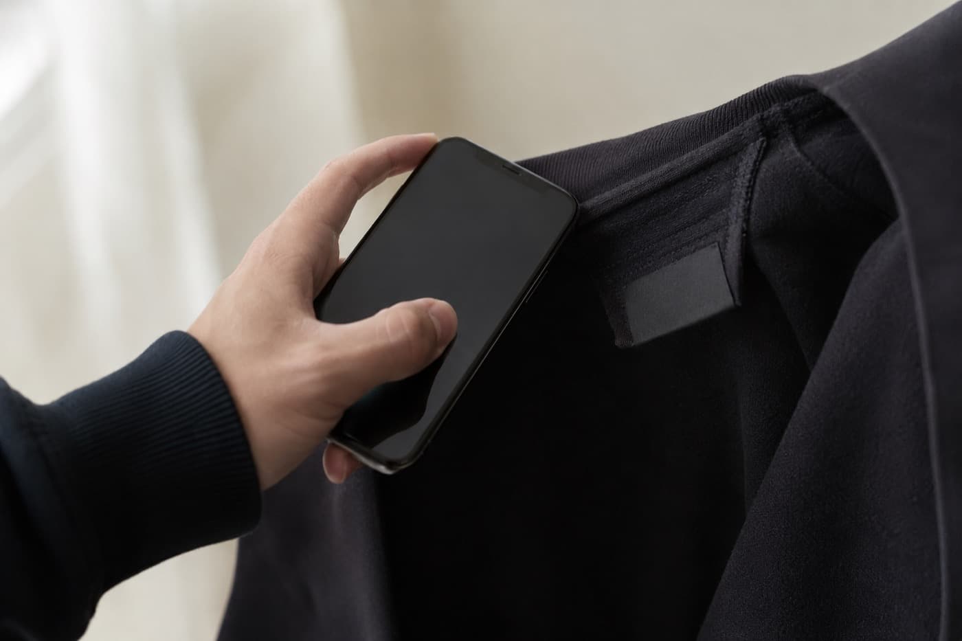 A hand holding a phone close to the care label sewn inside a dark garment.