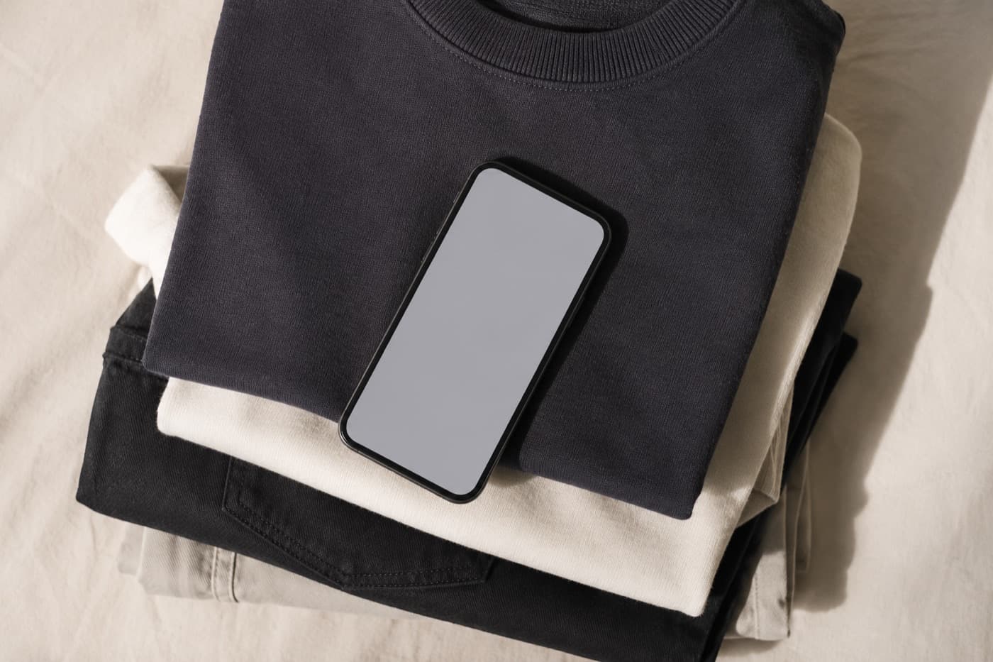 A phone lying face up on a stack of folded charcoal and off-white garments.